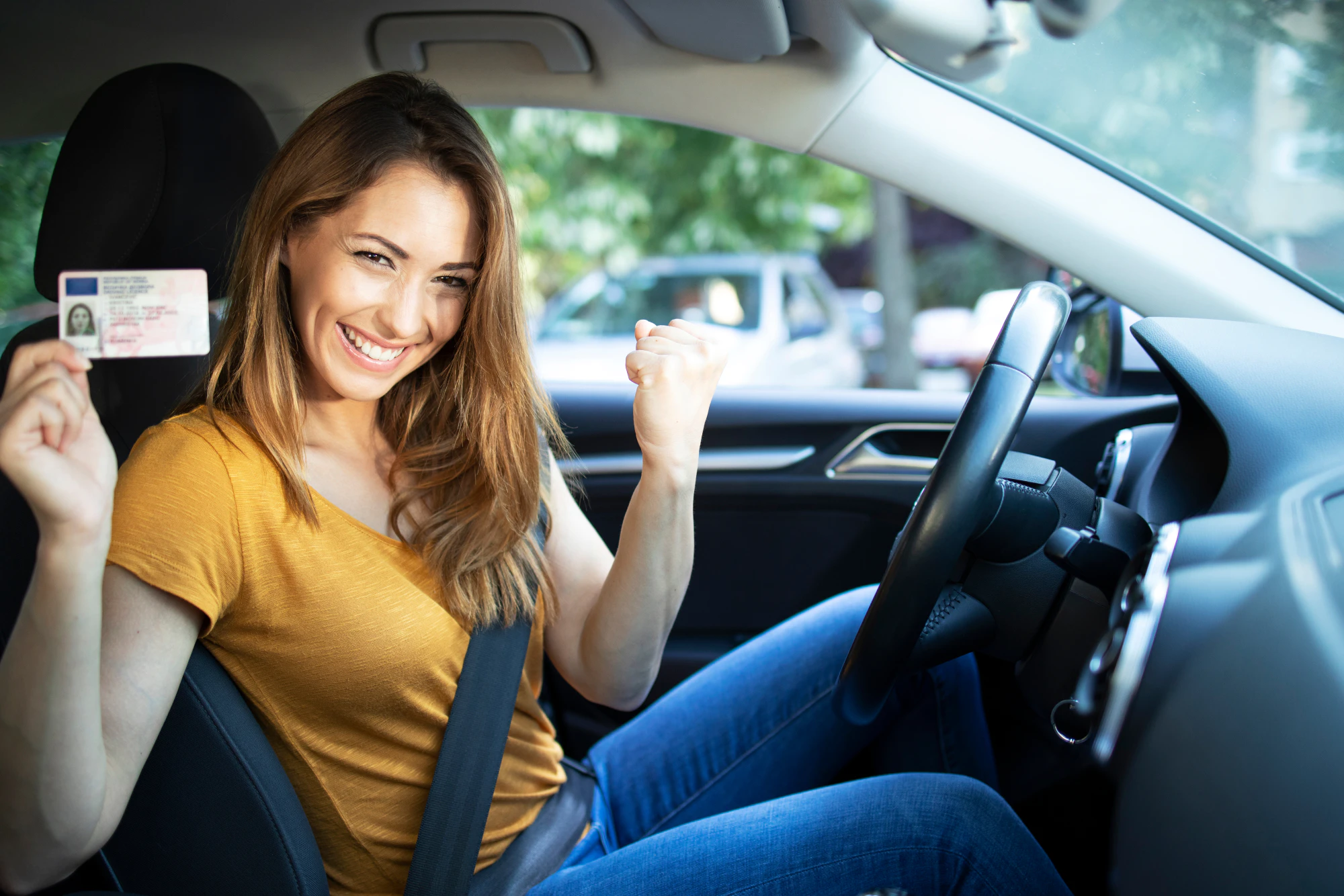 Young woman holding up her license in her car