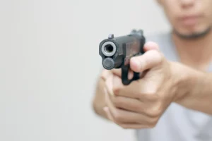 Out of focus man in a white t-shirt points a pistol toward the camera.
