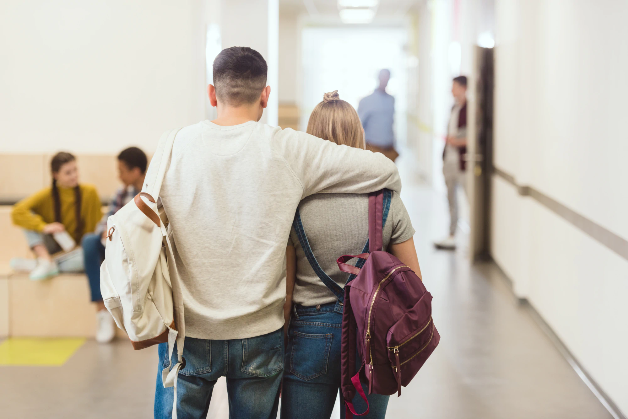 Student couple walking at school with their backpacks on, the man with his arm around the girl.