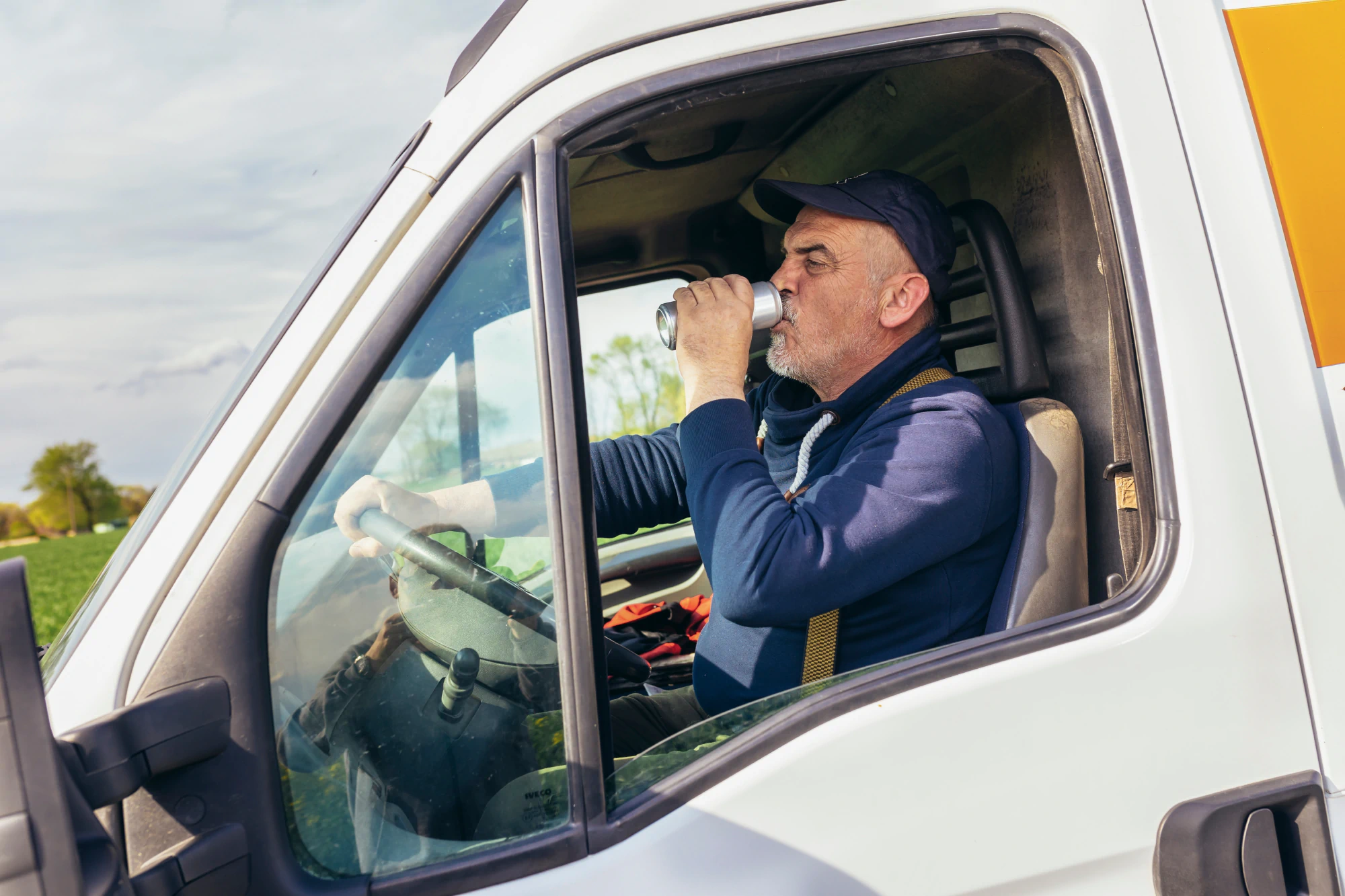 Older truck driver drinks beer behind the wheel of his box truck.