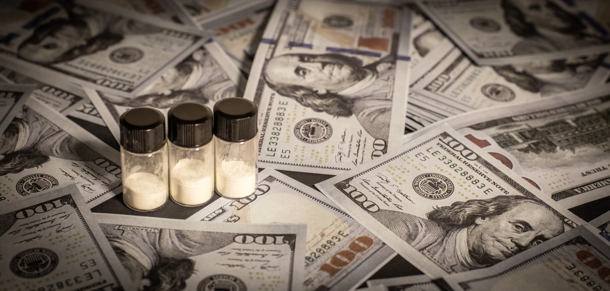 Vials of powdered drugs atop a table covered with $100 bills.