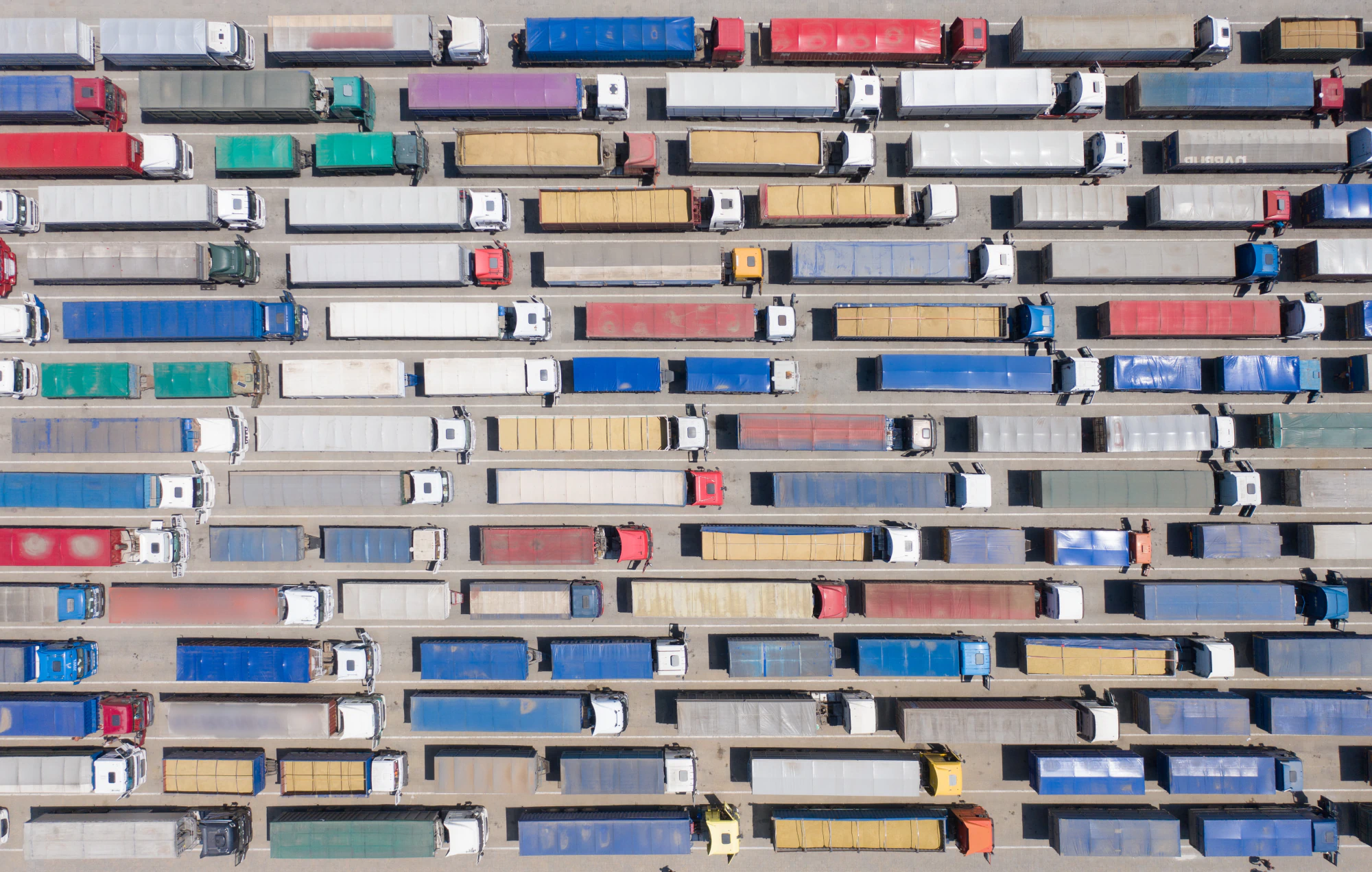 Overhead view of tens of multicolored trucks waiting for a border control checkpoint.