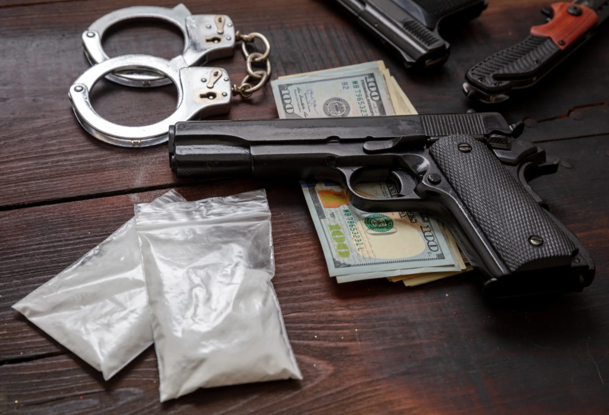 A gun, money, drugs, and handcuffs on a table