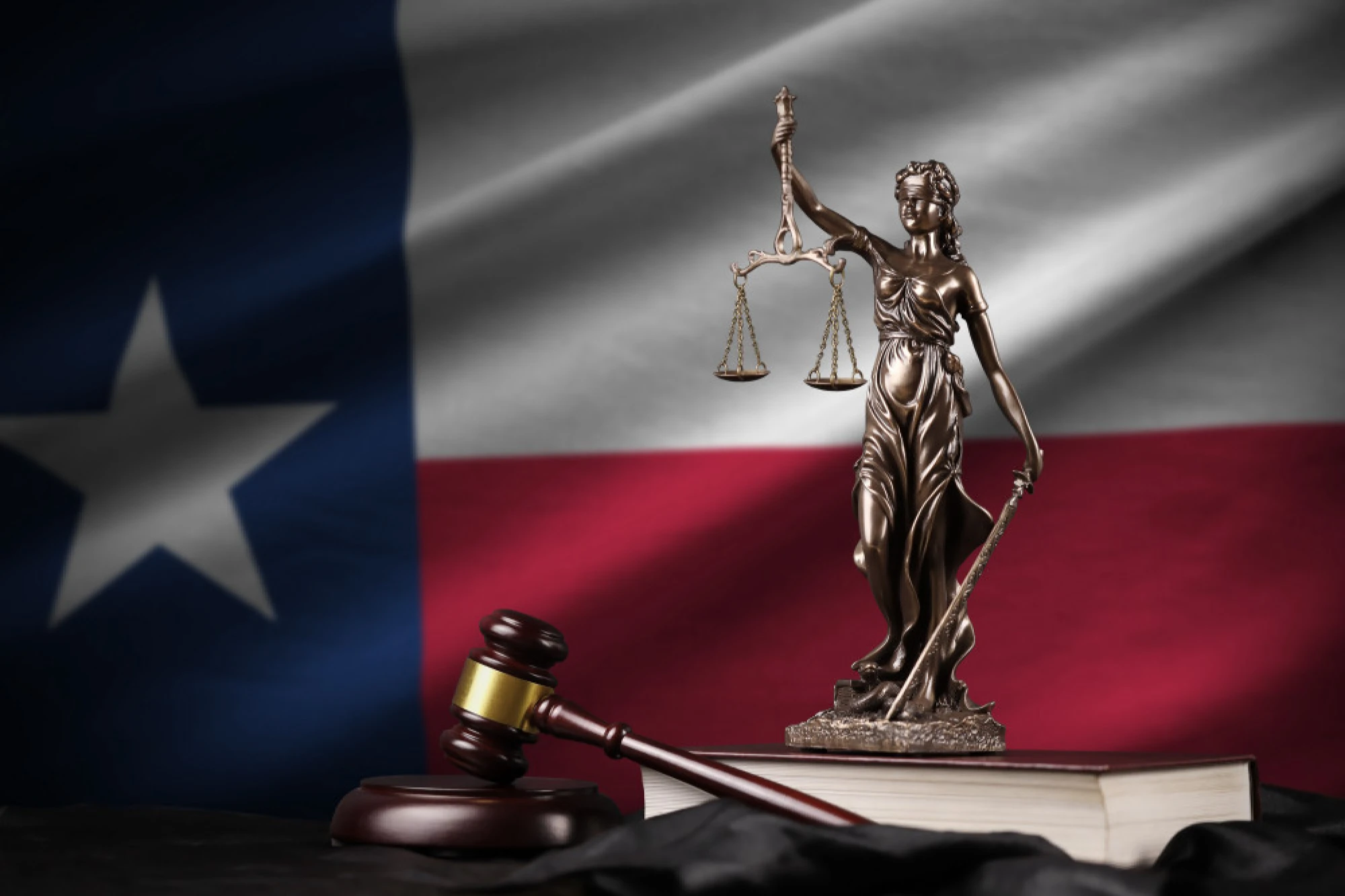 A gavel and a statue of Lady Justice in front of the Texas State flag
