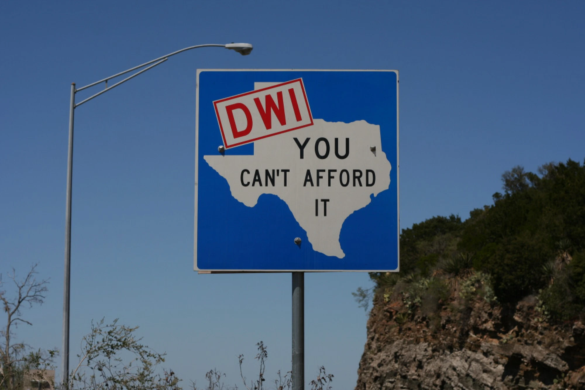 A street sign with an outline of the state of Texas and the words, “DWI, you can’t afford it.”