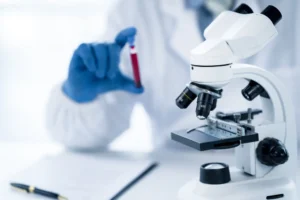 A doctor testing a vial of blood with a microscope