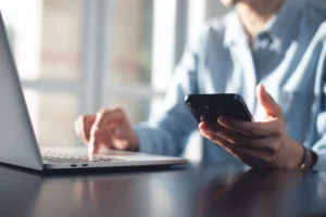 Businessman typing on his laptop while holding his phone