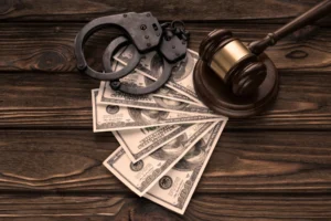A view of cash, handcuffs, and a judge’s gavel on a table.