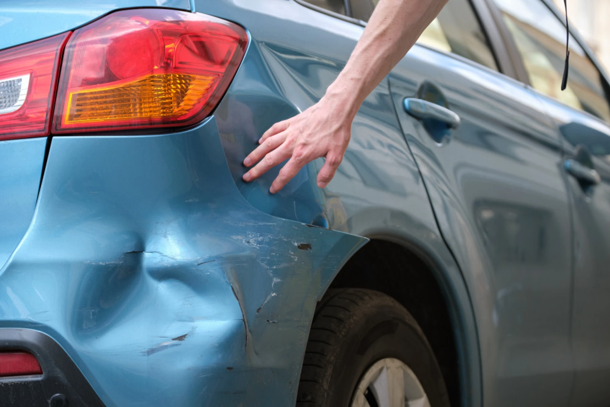A person examining the damage on his car from a hit and run
