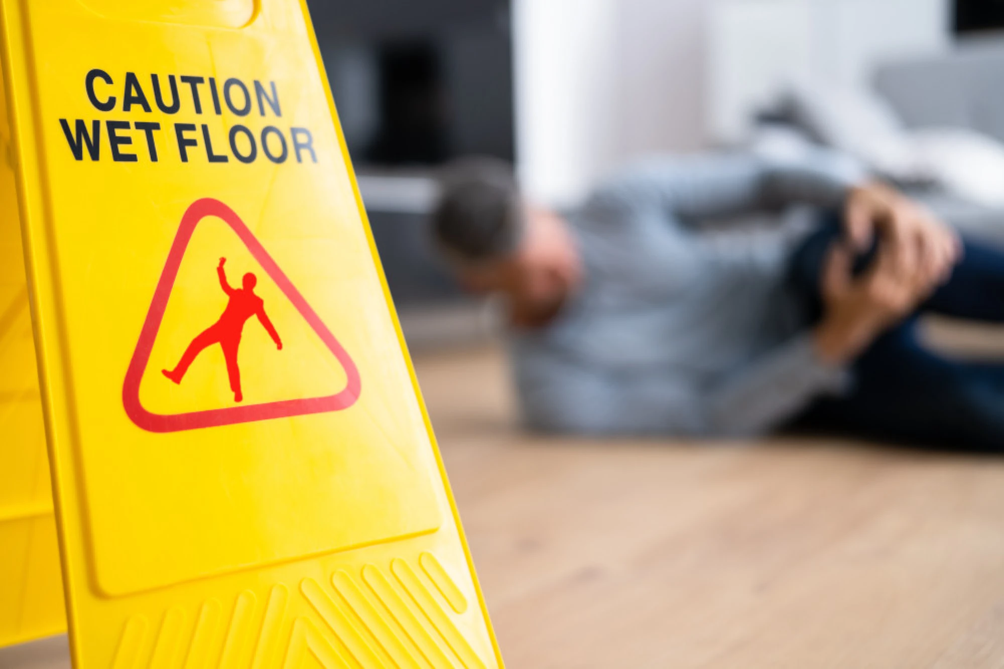 Close up view of a caution wet floor sign with an injured person in the blurred background