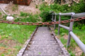 Una valla metálica oxidada que cuelga delante de unas escaleras peligrosas