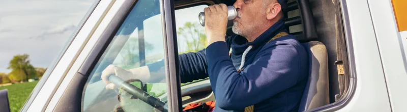 Older truck driver drinks beer behind the wheel of his box truck.