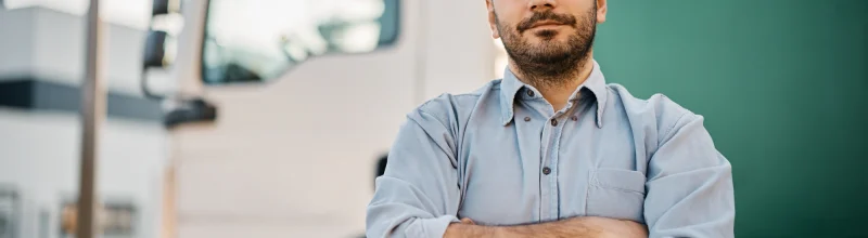 Truck driver standing in front of his truck looking at the camera with crossed arms.