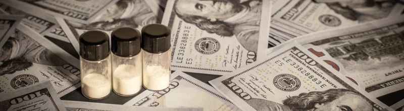 Vials of powdered drugs atop a table covered with $100 bills.