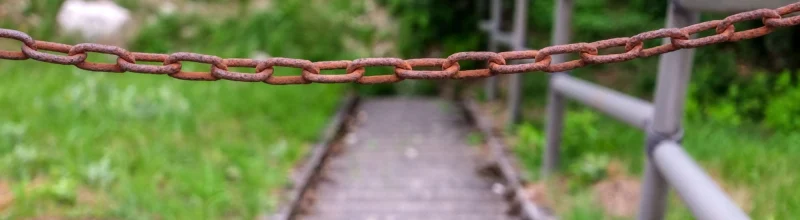Una valla metálica oxidada que cuelga delante de unas escaleras peligrosas