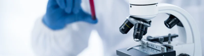 Un médico analiza un vial de sangre con un microscopio
