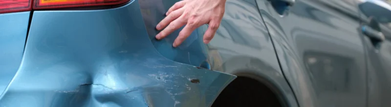 A person examining the damage on his car from a hit and run